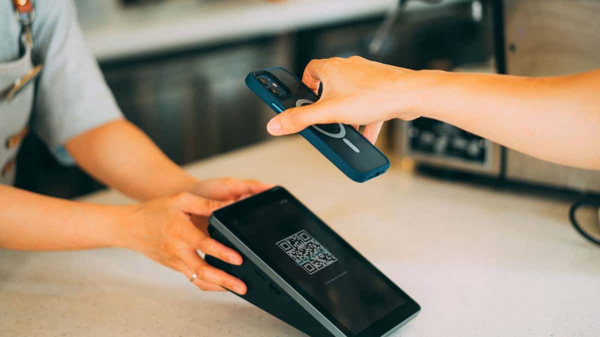 Cliente pagando con el teléfono frente a un lector de código QR en un mostrador